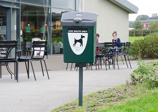 Fido™ 25 Dog Waste Bin in deep green with post mounted fixings in front of leisure facility entrance with seating outside