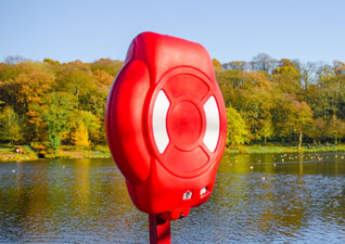 Guardian™ Lifebuoy Housing in red located by large park lake, surrounded by trees